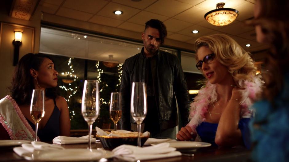 Iris looks over at a creepy guy who is standing over the table looking down at Caitlin.