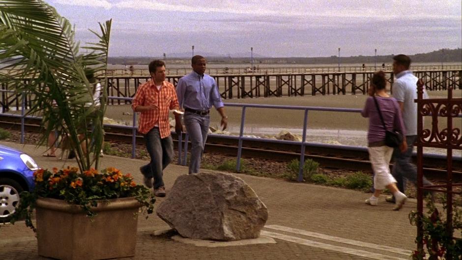 Shawn walks down the boardwalk with Gus while holding the terrible pineapple  upside-right cake.