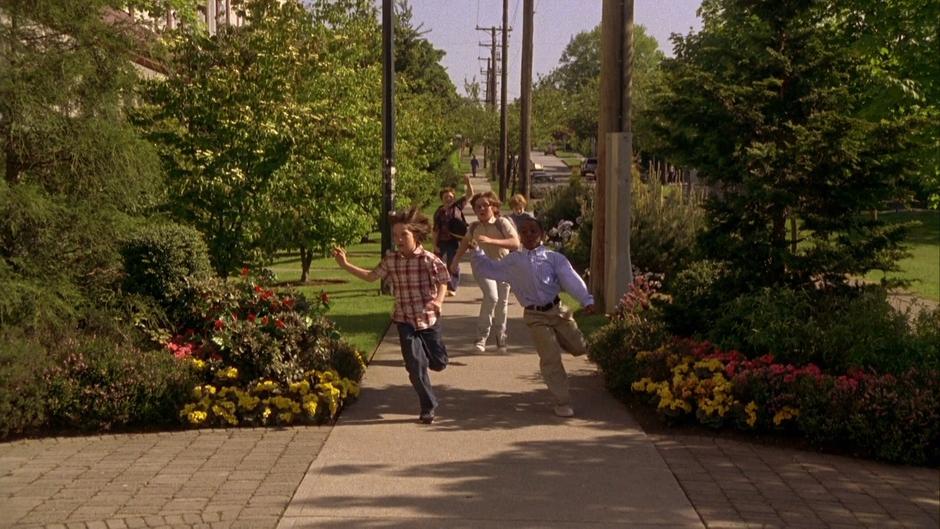 Shawn and Gus run down the sidewalk in front of a group of kids.