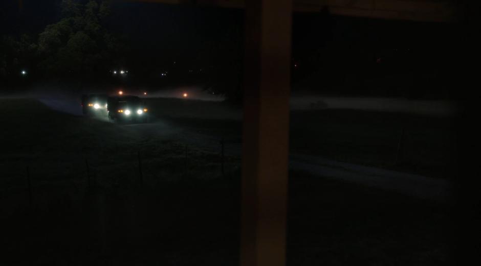 Two military trucks drive up to the house through the fog.