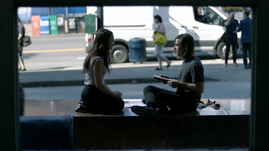 Julia and Quentin sit outside the library discussing their upcoming quest.