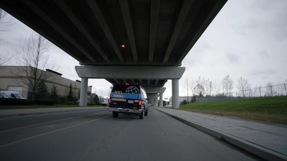 The stolen delivery van drives down the street under an elevated highway.