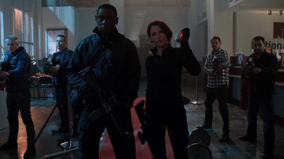 J'onn stands next to Alex as she prepares a red sun grenade to throw at Reign while surrounded by other DEA agents.
