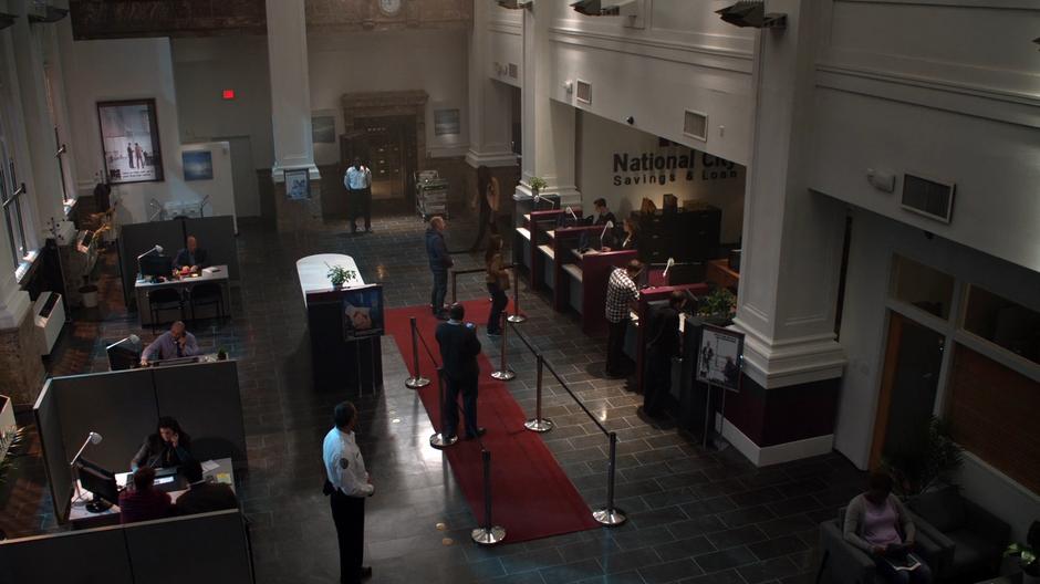 Establishing shot of patrons and employees milling around in the bank.