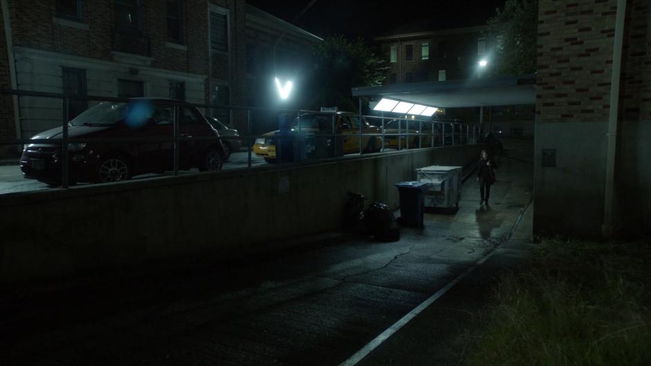 Quentin walks through the alley past some dumpsters.