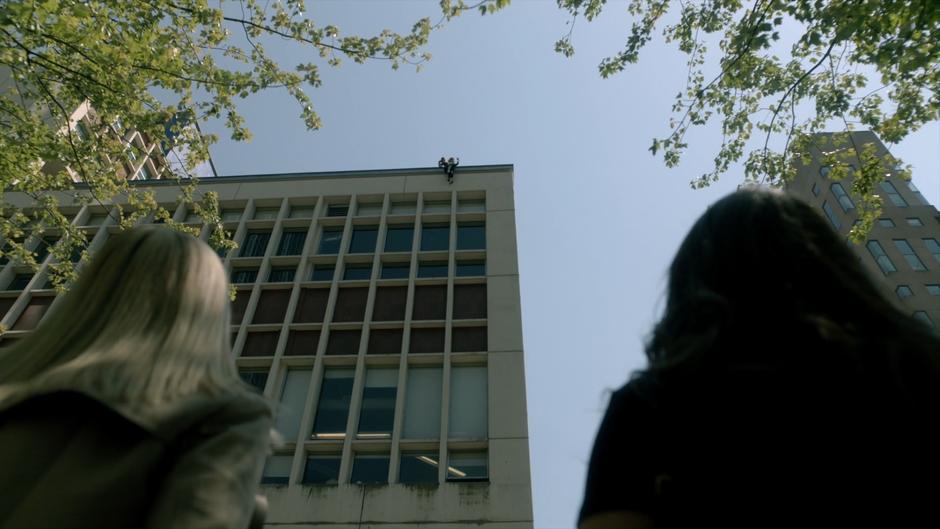 Alice and Julia look up at the building as Quentin grabs Professor Lipson as she falls.