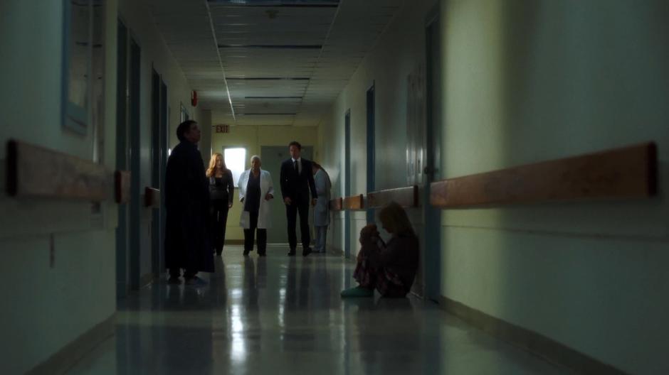 Scully and Mulder walk down the hallway with Dr. Babsi Russel while asking about the recent cases.