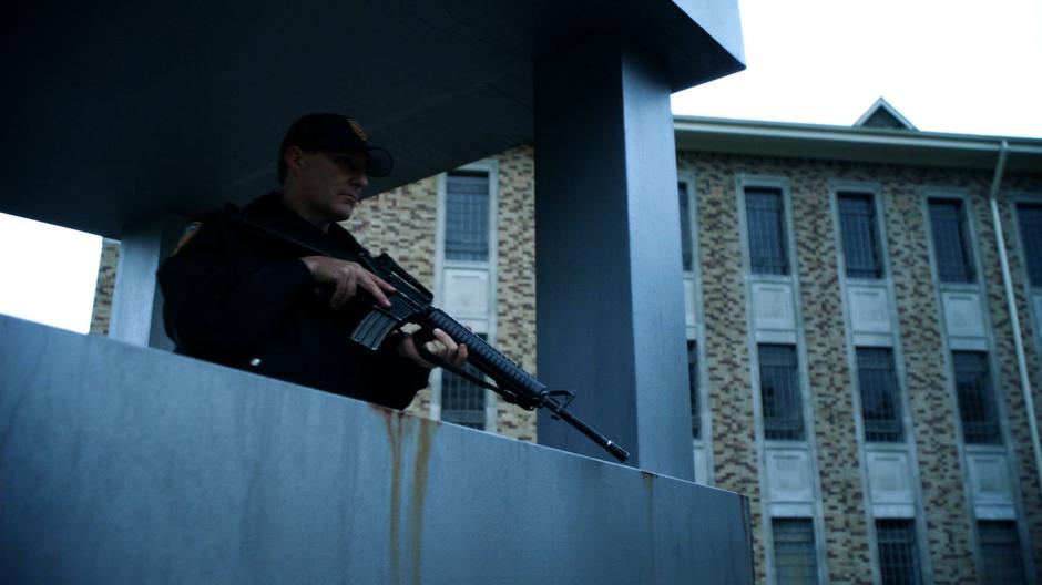 A guard watches the yard from a tower with a gun.
