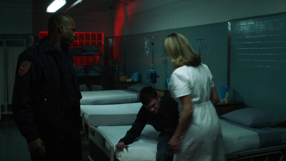 A guard helps Axel Walker into one of the infirmary beds and Zoey Clark comes over in a nurse's outfit to examine him.