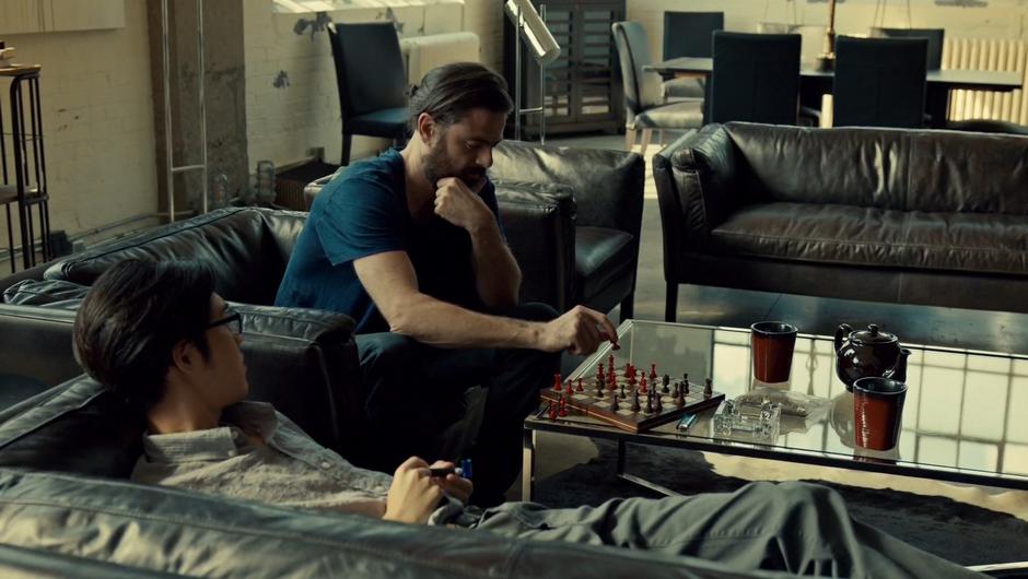 Des makes a chess move while Joshua smokes on the couch.
