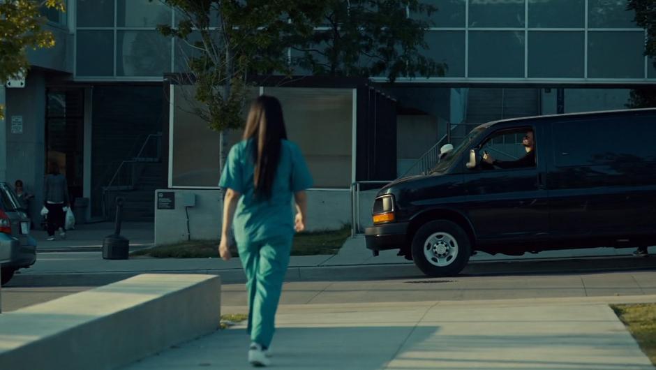 Annie walks back to the hospital while a unmarked black van sits on the street.