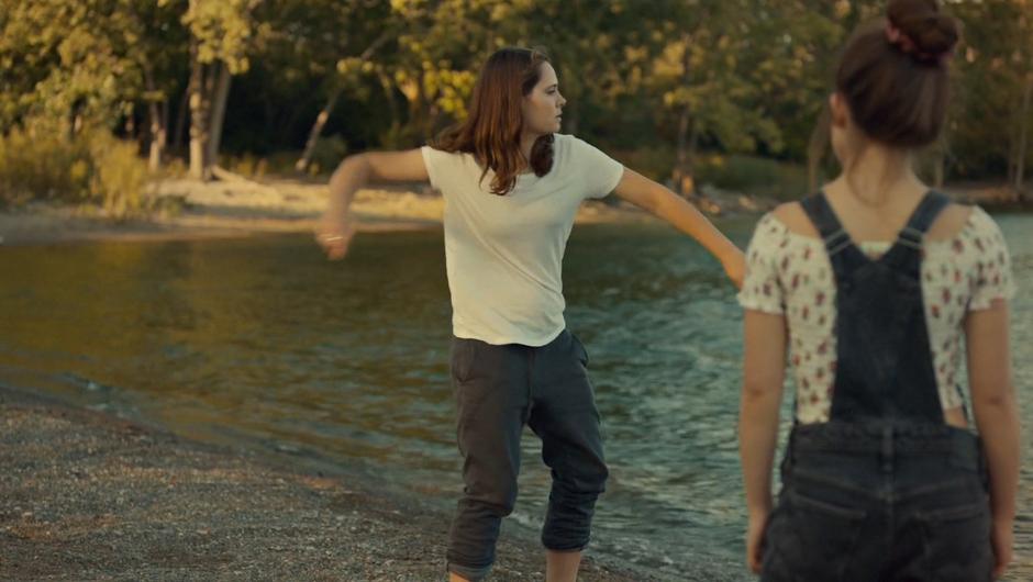 Jess skips a stone across the water while Naomi watches.