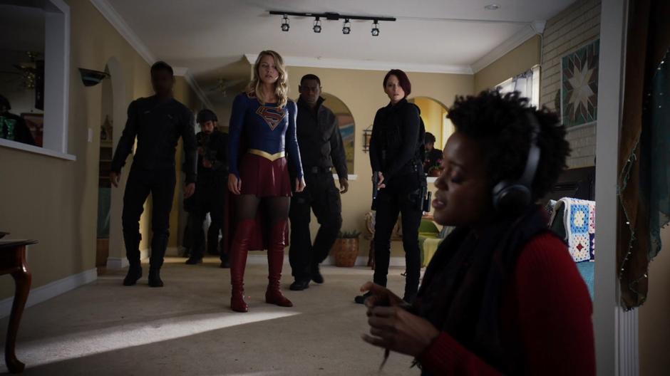 Kara, J'onn, Alex, and the DEO team look at Julia Freeman who is obliviously listening to her music.