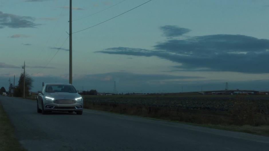 Scully and Mulder drive down the road towards town.