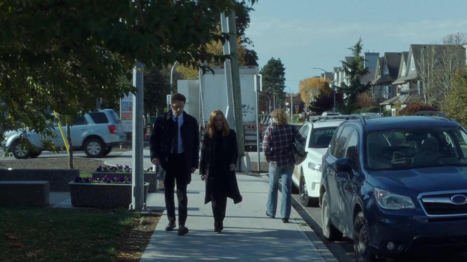 Mulder and Scully walk down the sidewalk on their way back to the car.