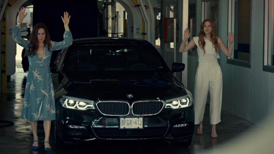 Mary and Olivia walk out of the car with their hands up.