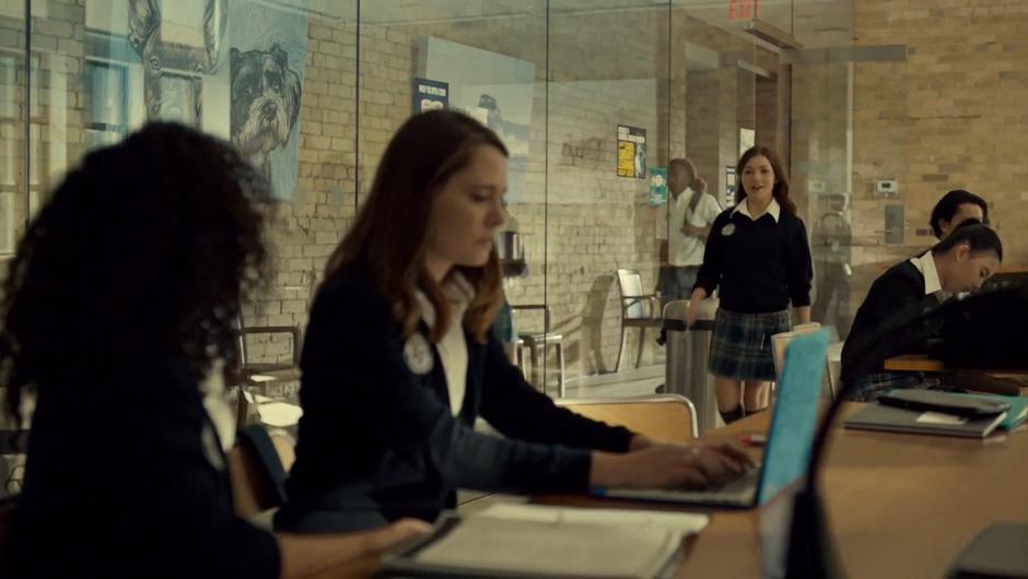 Naomie walks over to Heather and Jess while they are studying at a table.
