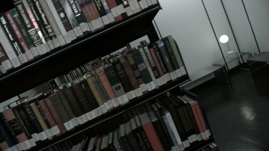 Penny sneaks behind some bookshelves after seeing two librarians.