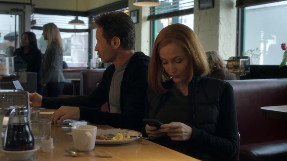 Mulder and Scully sit at the diner's bar lost in their phones.