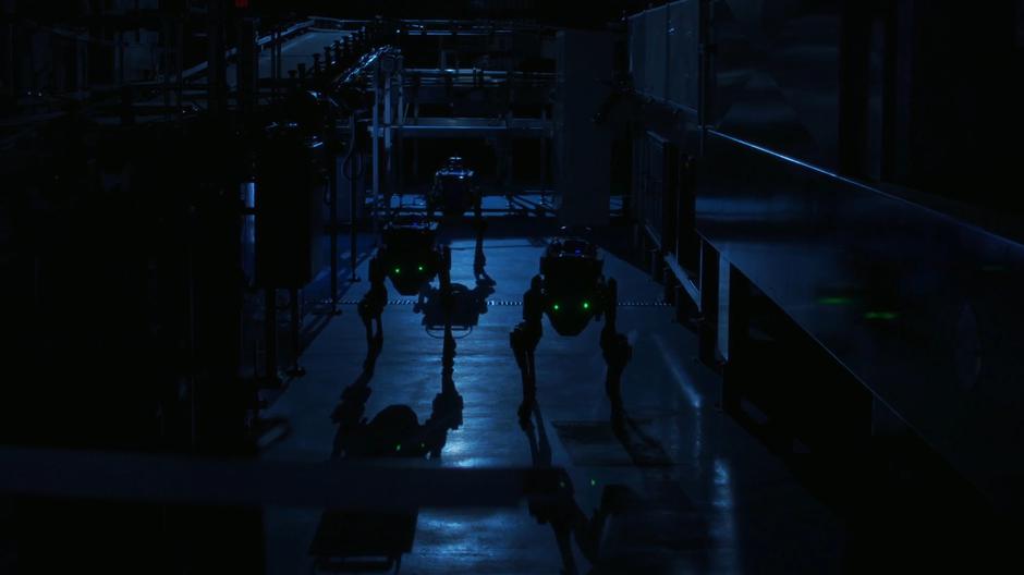 Three Bostom Dynamics dog robots walk ominously through the factory.