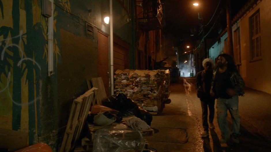 A couple of homeless people walk down the alley.