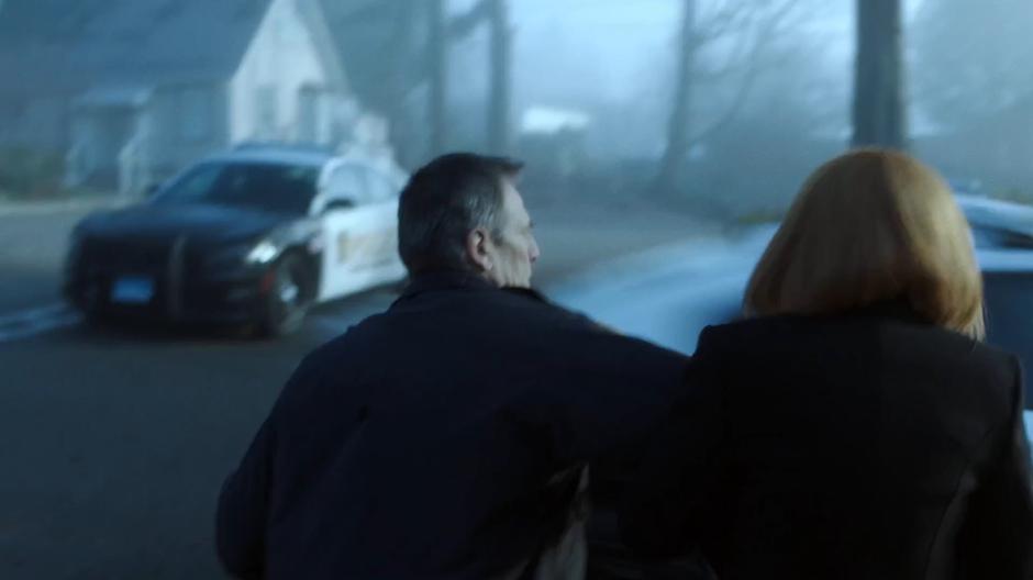 Chief Strong pushes Scully back as Officer Eggers speeds past in a squad car.