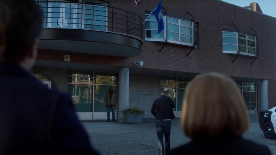Officer Wentworth stands in the shadows across from the courthouse getting Mulder and Scully's attention.