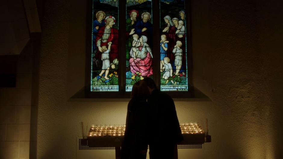 Scully whispers in Mulder's ear next to the prayer candles.
