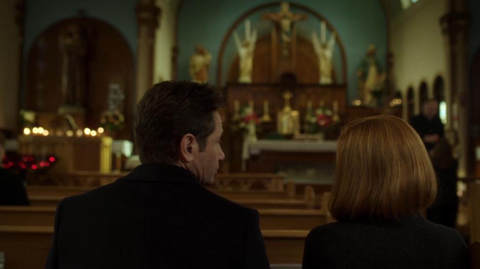 Mulder and Scully talk while sitting in the pews.