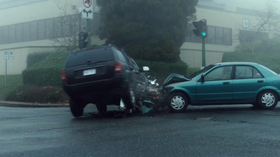 Two cars collide in the middle of the intersection while all the lights show green.