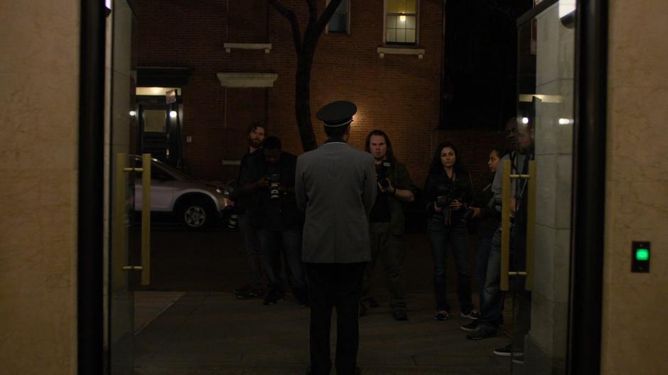 The doorman of the building holds back the crowd of paparazzi.