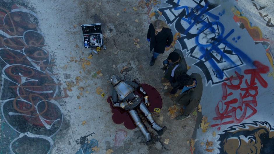 Liv, Clive, and Ravi gather around the corpse in a suit of armor.