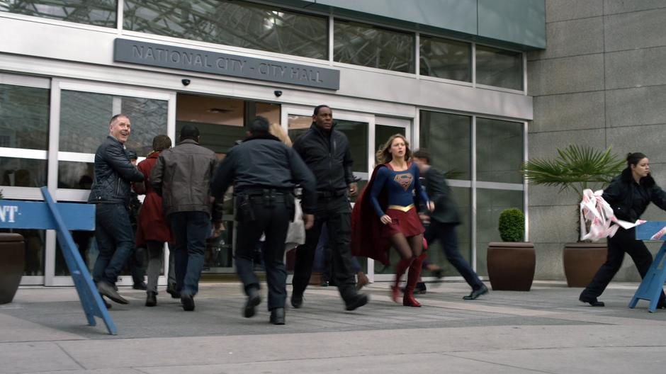 J'onn and Kara run outside after a forcefield goes up around the building.