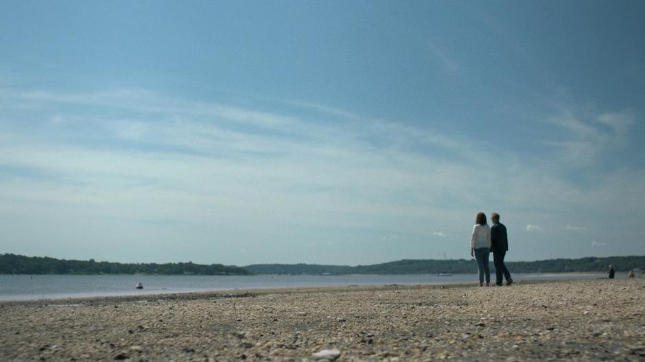 Alisa and Malus walk down onto the beach and look out over the water.