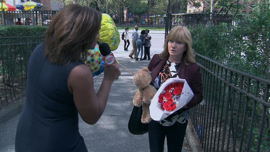 The news reporter Thembi Wallace ambushes Dorothy out front of the hospital as she is arriving with a stuffed bear, flowers, and balloons for Trish.