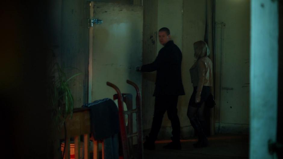 Two well-dressed people enter a mysterious door at the back of the shop.