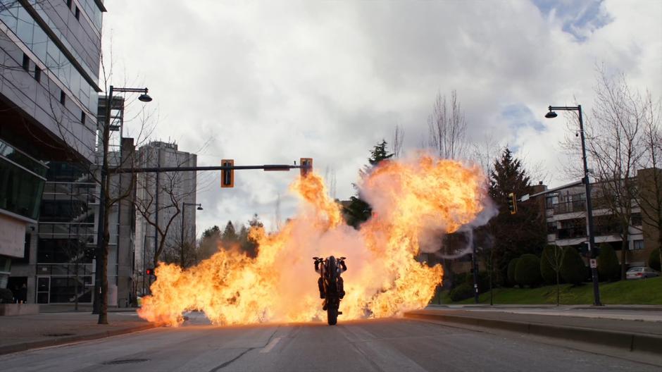 James rides his motorcycle through an explosion.