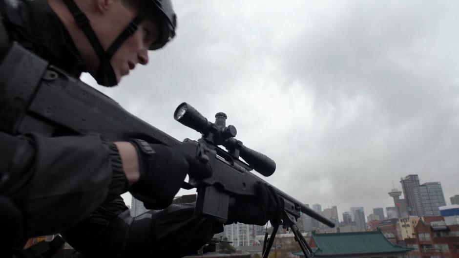 A DEO agent sets up his sniper rifle at the edge of the roof.