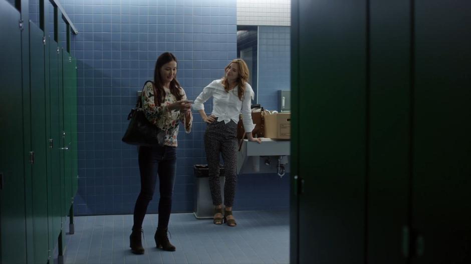 Hannah smiles at Carmen in the bathroom while she talks to Dave on the phone.