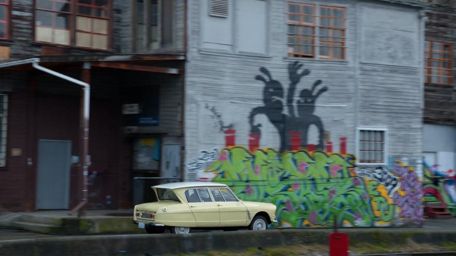 Lambert's car drives down the alley past a graffiti-covered wall.