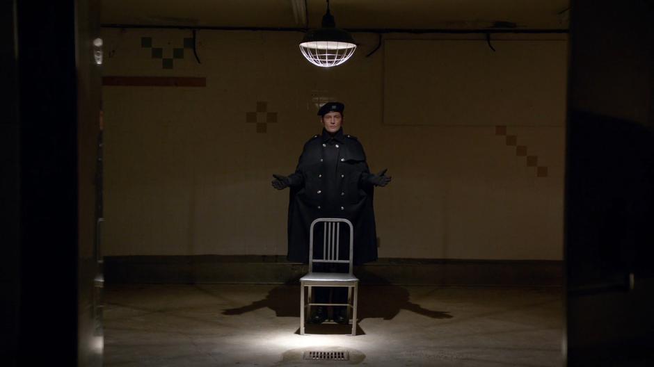 Lambert waits in the interrogation room behind a metal chair.