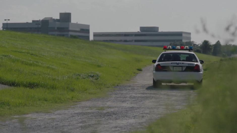 A police car sits on a dirt road behind some buildings.