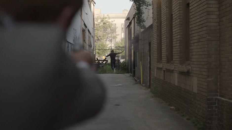 Tyrone leaps into the air as Connors fires at him from the mouth of the alley.