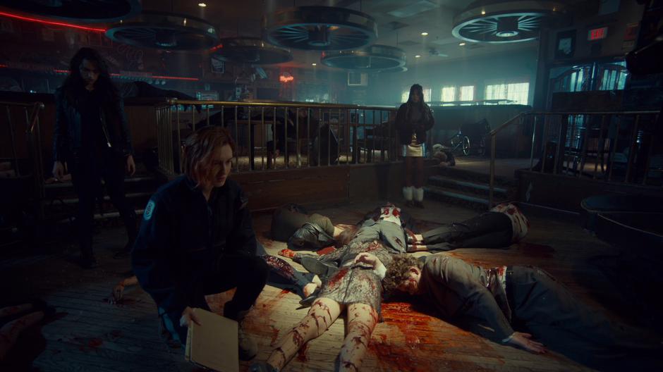 Nicole kneels over the slaughtered bodies while Wynonna and Waverly look around the scene.