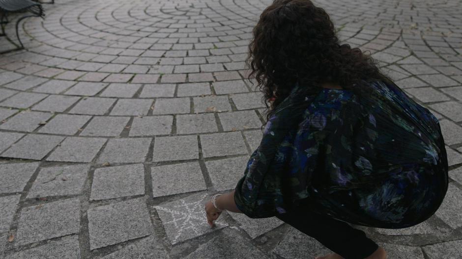 Auntie Chantelle looks up after making a chalk marking on the tiles of the square.