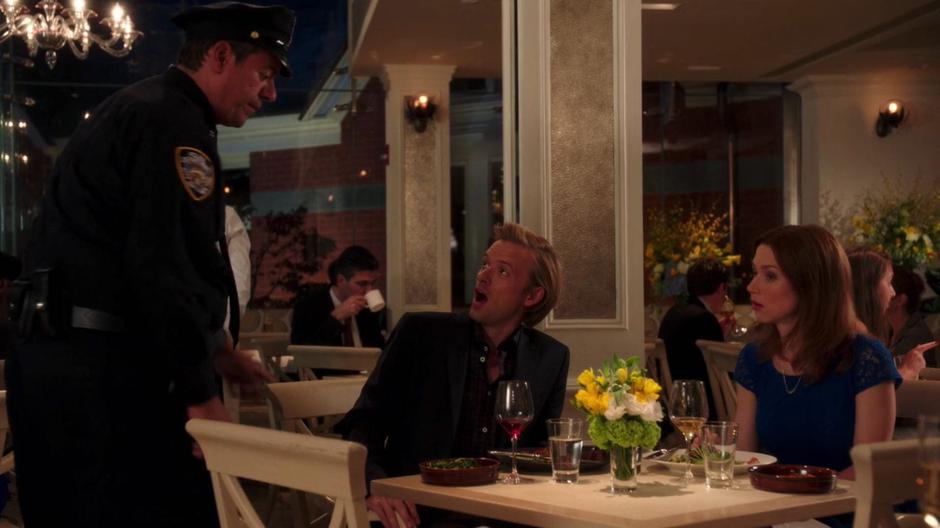 Logan looks up in suprise at the police officer who approached the table where he is haiving dinner with Kimmy.
