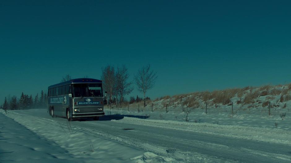 The bus drives down a snowy road into town.