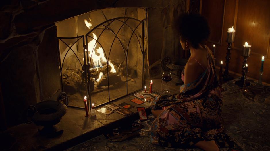Kate sits half-dressed in a robe with her tarot cards in front of the fire.