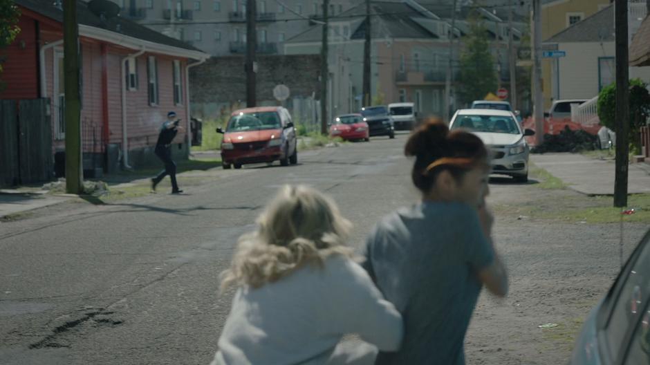 Tandy pushes Mina behind a car as the Roxxon fixer shoots at them from down the street.
