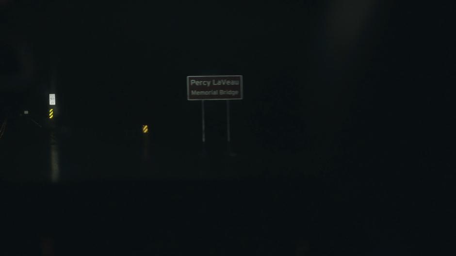 The car drives past the sign for the bridge in the dark.